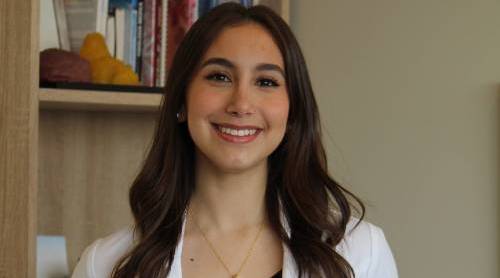 Melissa Fernandez smiling wearing a lab coat while standing in front of a bookcase